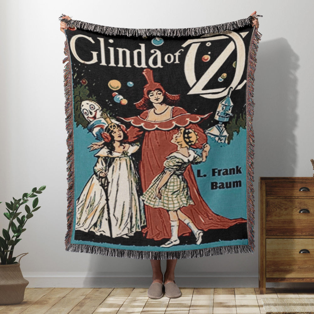 Glinda of Oz woven throw blanket showing the vintage book cover with Glinda, Dorothy, and Ozma