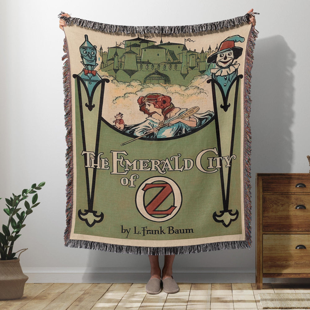 The Emerald City of Oz woven throw blanket showing the vintage cover with the city skyline, Tin Man, and Scarecrow