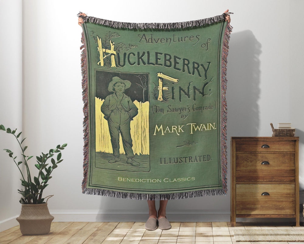 Huckleberry Finn woven throw blanket showing the classic green book cover with Huck at the fence